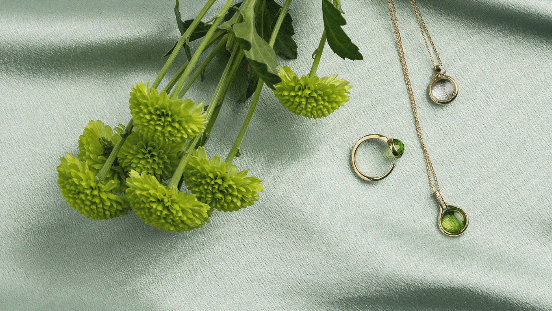 A gold necklace and ring set with Selah Stones, resting on fabric beside green flowers